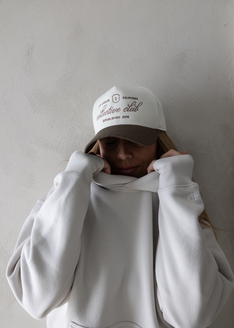 Woman wearing a cozy neutral loungewear set with sweatsuit and sweatpants, paired with a beige streetwear baseball cap by stitched apparel branded as STCHD