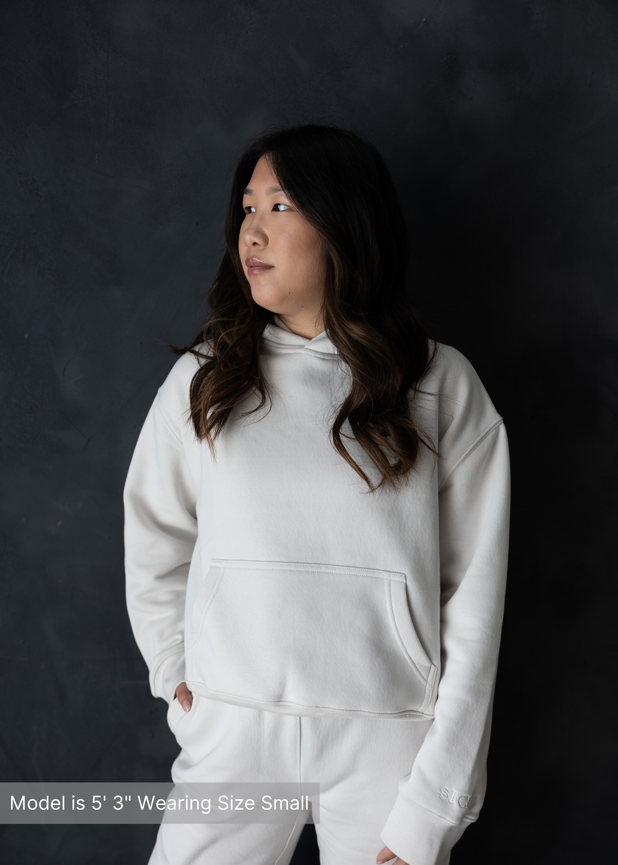 Front view of woman in neutral loungewear hoodie set by stitched apparel branded as stchd, against a dark backdrop, cozy and relaxed fit
