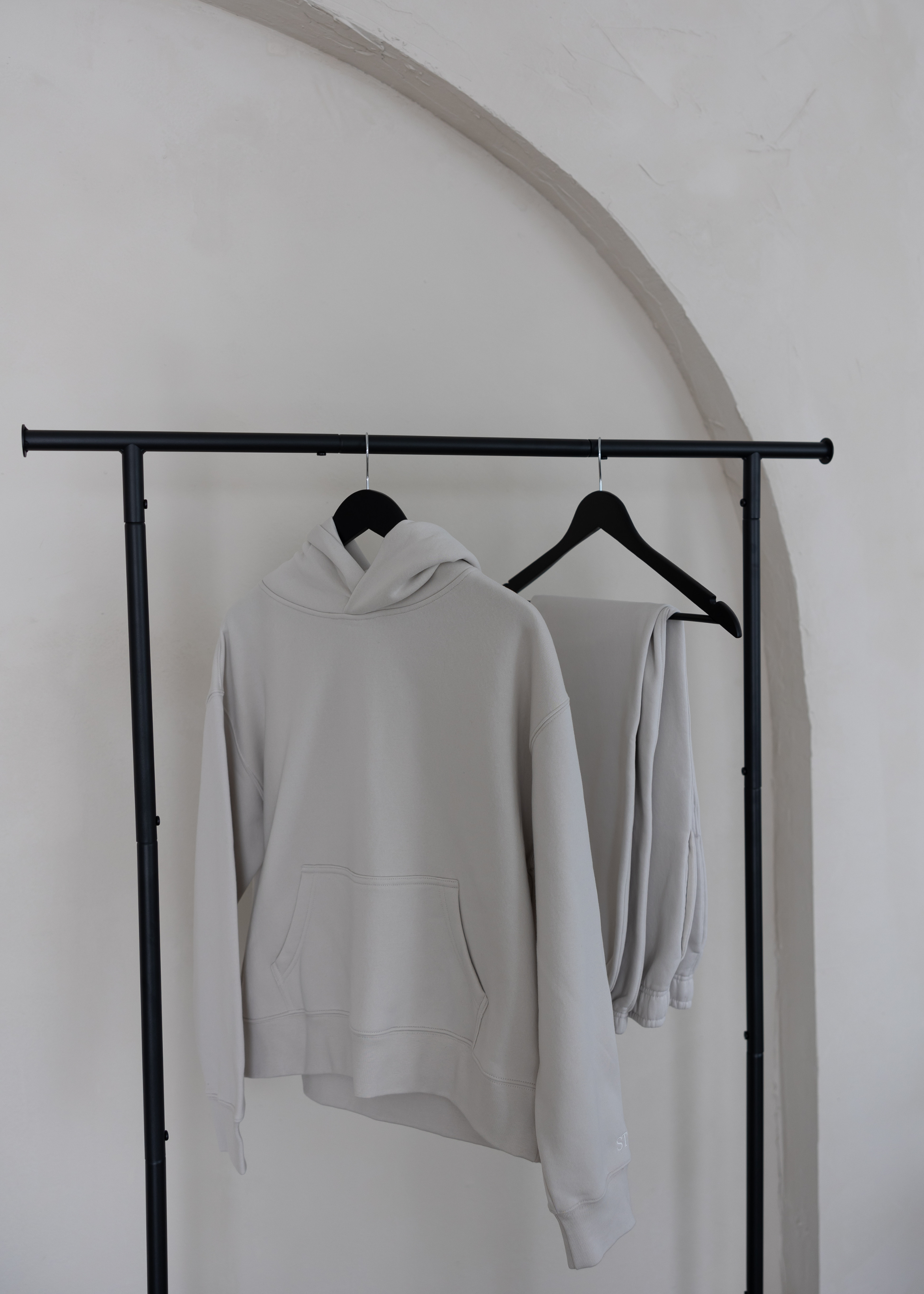 Neutral women’s loungewear set with hoodie and sweatpants by stitched apparel by STCHD, hanging on black clothing rack in minimalist setting