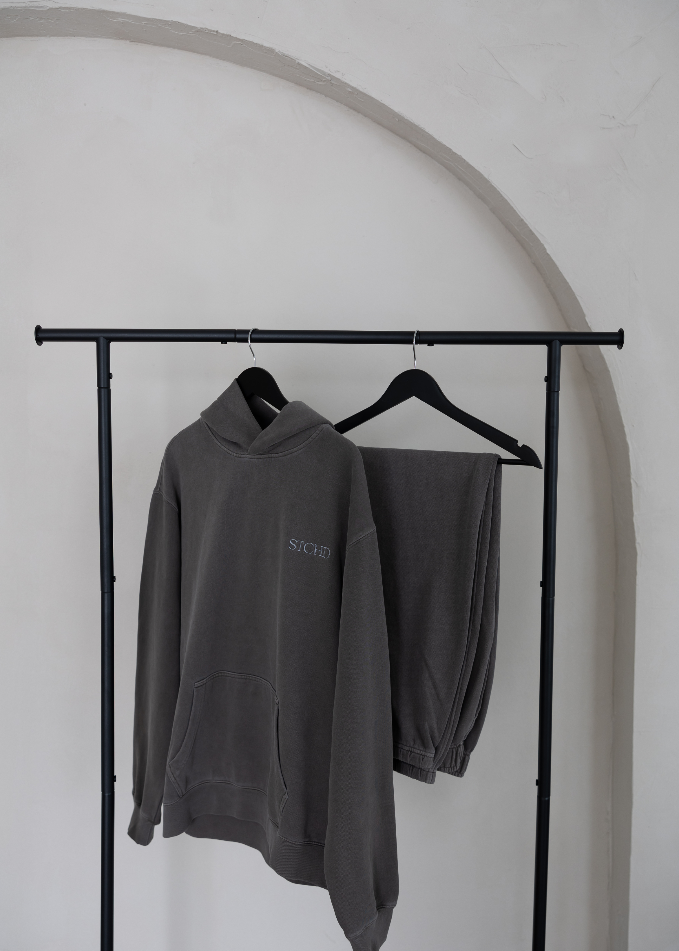Washed grey STCHD men’s hoodie and sweatpants loungewear set hanging on black minimalist clothing rack.