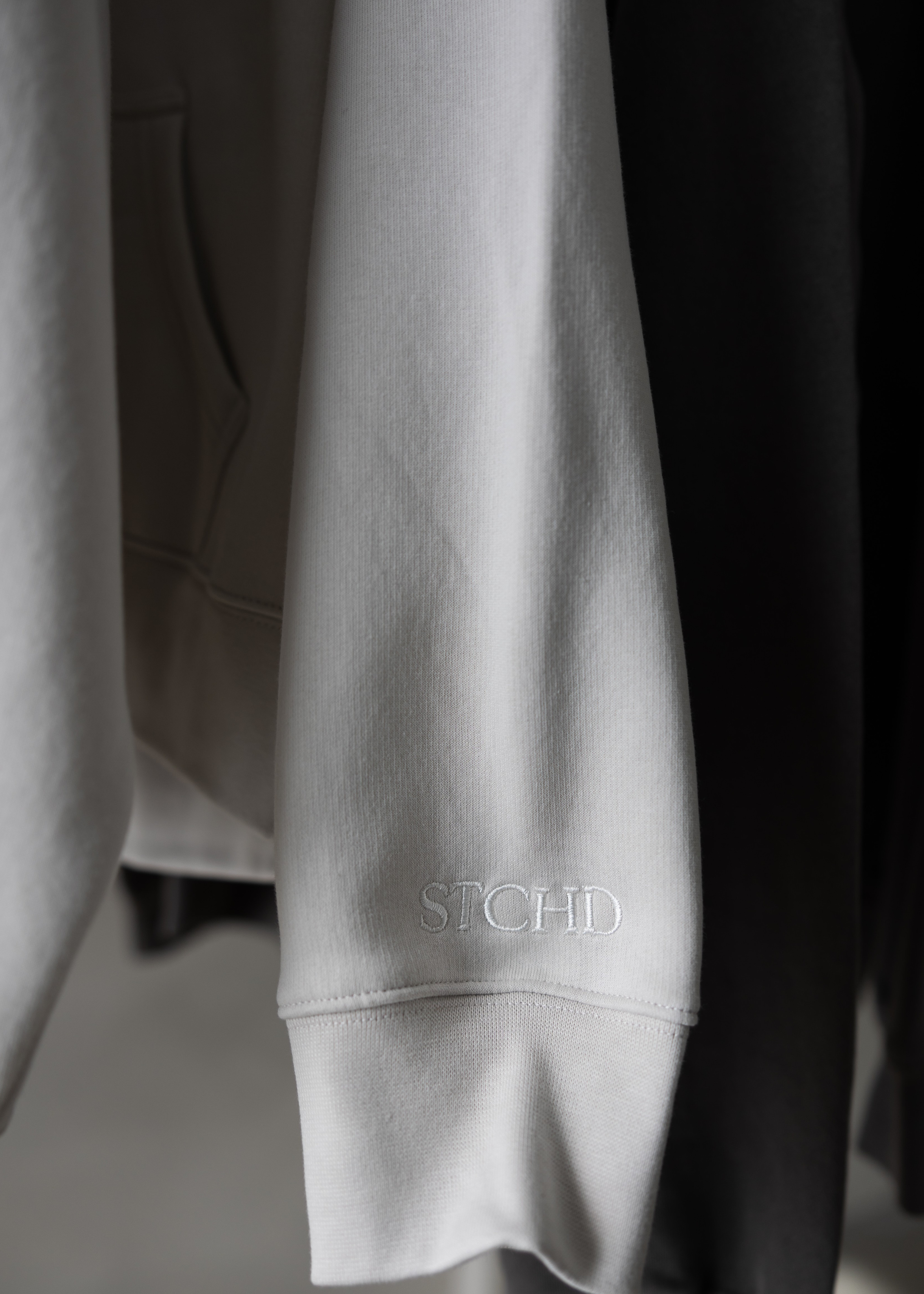 Close-up detail of embroidered STCHD logo on sleeve hem of neutral women’s hoodie.